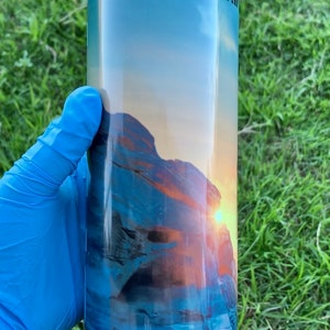 May include: A blue and orange tumbler with a white lid. The tumbler features a graphic of a sunset over a rocky landscape and the text "Star Wars The Mandalorian".