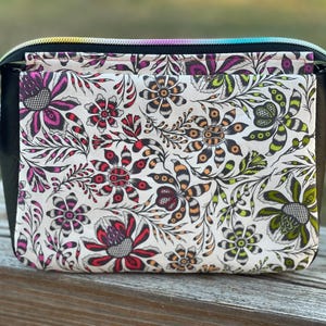 May include: A small black zippered pouch with a white floral print. The print features black, red, green, and yellow flowers with intricate details.