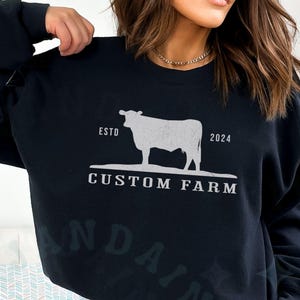 Puede incluir: Sudadera negra con una silueta blanca de una vaca y el texto "ESTD 2024 CUSTOM FARM".