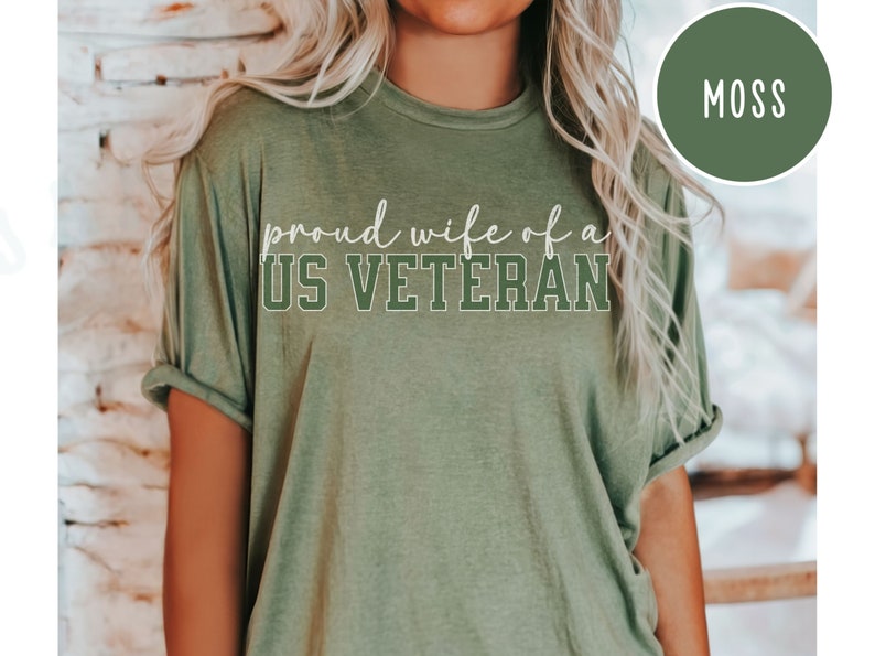 Puede incluir: Camiseta verde musgo con el texto "proud wife of a US VETERAN" en escritura blanca y letras de bloque. La camiseta tiene mangas enrolladas y cuello redondo. Un gr&aacute;fico circular en la esquina superior derecha dice "MOSS".