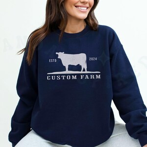 Puede incluir: Sudadera azul marino con una silueta blanca de una vaca y el texto "ESTD 2024 CUSTOM FARM".