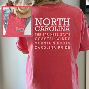 May include: A red t-shirt with the text "NORTH CAROLINA" and other phrases in white. An inset image shows a matching shirt with "NC" on it. The shirt is a casual wear item.