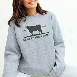 Puede incluir: Una sudadera gris con una silueta negra de una vaca y el texto "ESTD 2024 ARMSTRONG FARMS".