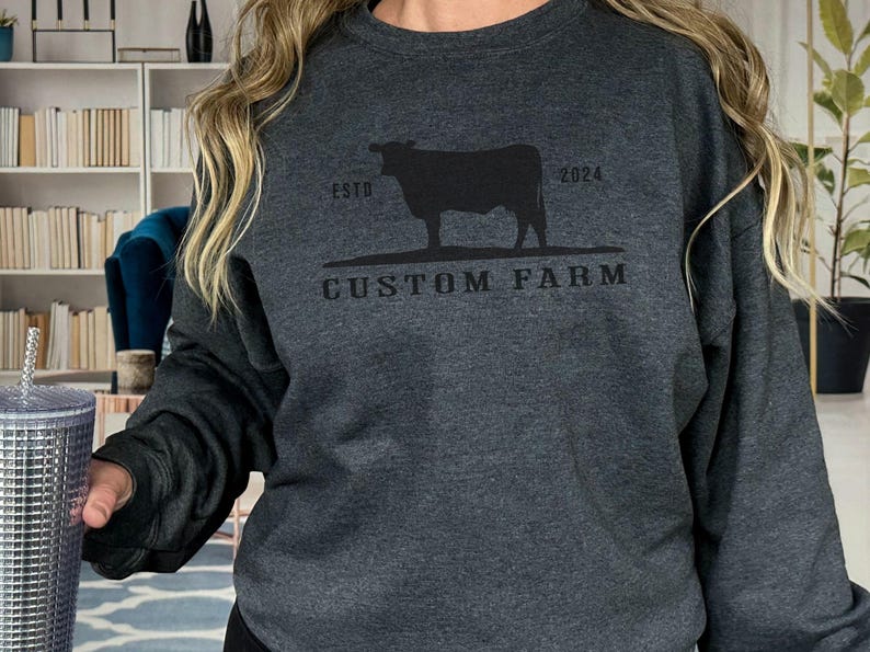 Puede incluir: Una sudadera gris oscuro con una silueta negra de una vaca y el texto "ESTD 2024 CUSTOM FARM".