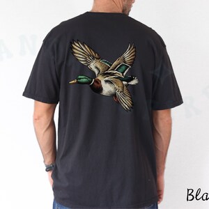 Może przedstawiać: Czarny t-shirt z grafiką lecącego dzikiego kaczora na plecach. Kaczor jest brązowy, zielony i biały.