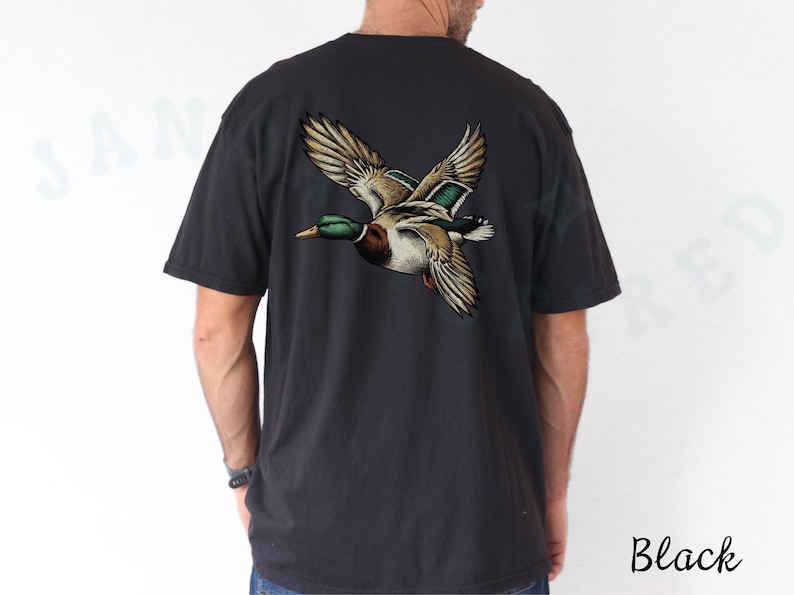 Może przedstawiać: Czarny t-shirt z grafiką lecącego dzikiego kaczora na plecach. Kaczor jest brązowy, zielony i biały.
