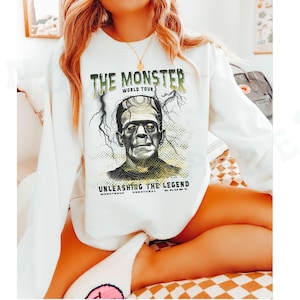 May include: White sweatshirt with a graphic print of Frankenstein's monster. The text on the sweatshirt reads 
