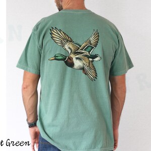 Może przedstawiać: Jasnozielony t-shirt z grafiką lecącego dzikiego kaczora na plecach.