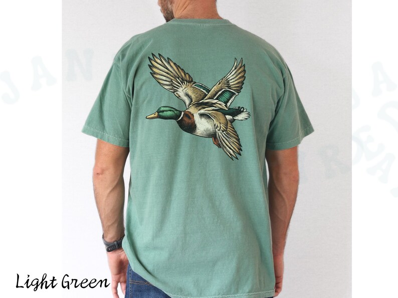 Może przedstawiać: Jasnozielony t-shirt z grafiką lecącego dzikiego kaczora na plecach.