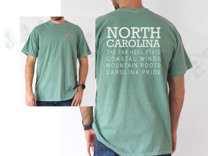May include: Sage green t-shirt featuring "NC" embroidery on the front and "NORTH CAROLINA" printed on the back, with state-related text. The shirt is short-sleeved and has a crew neck.