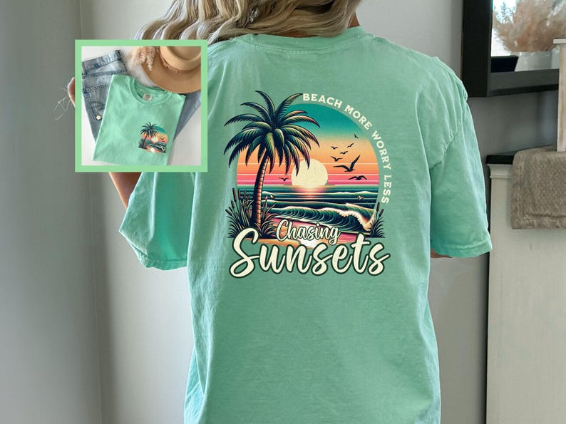 May include: A light green t-shirt with a graphic print of a palm tree, sunset, and ocean waves. The text "Beach More Worry Less" is printed in a circle around the graphic. The text "Chasing Sunsets" is printed below the graphic.