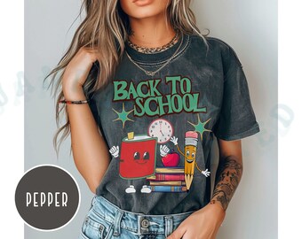 May include: A gray t-shirt with the text "Back to School" in green letters. The shirt features a cartoon illustration of a pencil, a book, a clock, and a red can with a smiling face.