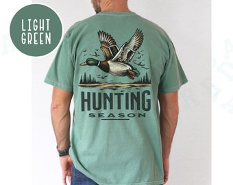 May include: A light green t-shirt with a graphic of a flying duck and the text "Hunting Season".