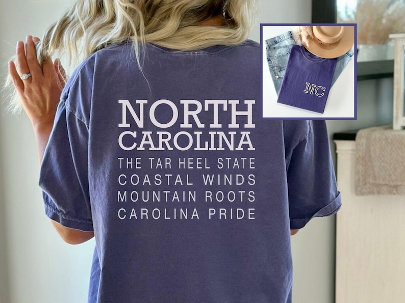 May include: A blue t-shirt with the words "NORTH CAROLINA" and other phrases printed in white. An inset image shows a similar shirt with "NC" embroidered on it, along with jeans and a hat. Clothing.