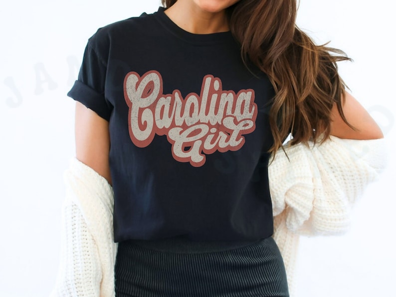 May include: A black t-shirt with a vintage-style graphic that says "Carolina Girl" in red and white lettering.