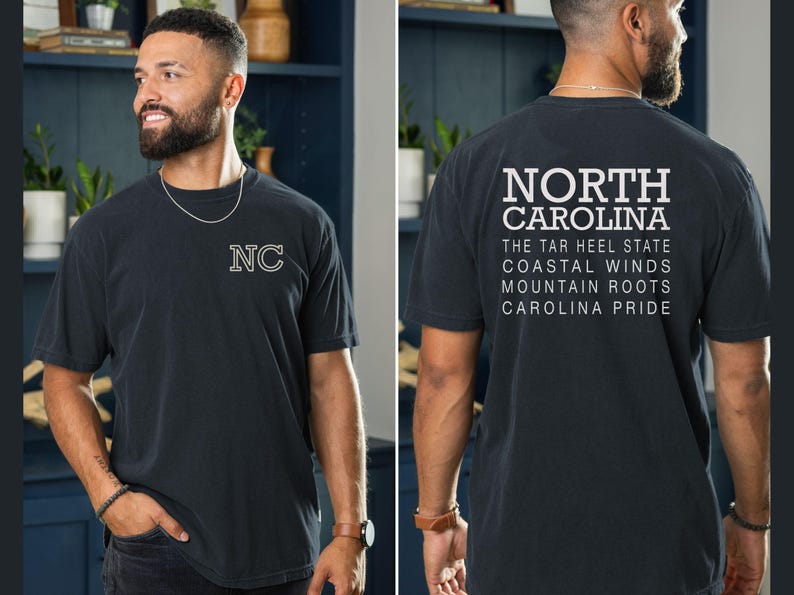 May include: Dark grey t-shirt with "NC" embroidered on the front. The back of the shirt features the words "NORTH CAROLINA" above text that reads "THE TAR HEEL STATE, COASTAL WINDS, MOUNTAIN ROOTS, CAROLINA PRIDE."