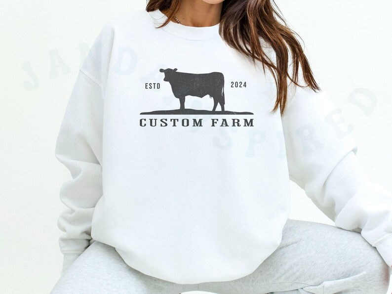 Puede incluir: Sudadera blanca con una silueta negra de una vaca y el texto "ESTO 2024 CUSTOM FARM".