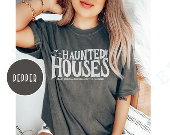 May include: A dark gray t-shirt with a white graphic that says "Haunted Houses" with a flock of white birds flying above the text. The text below the graphic says "Ready to roam the realm of the haunted."