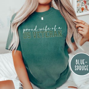 Puede incluir: Una camiseta de color verde azulado con el texto "proud wife of a US VETERAN" en letras blancas y verdes. La camiseta es de estilo casual y c&oacute;modo, perfecta para el uso diario. La camiseta est&aacute; etiquetada como "BLUE-SPRUCE".