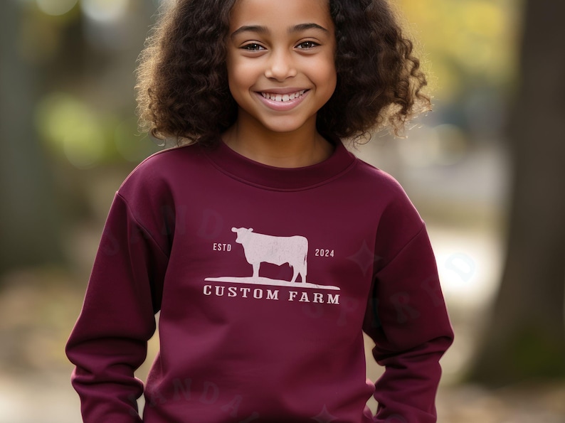 Puede incluir: Una sudadera color burdeos con una silueta blanca de una vaca y el texto "ESTD 2024 CUSTOM FARM".