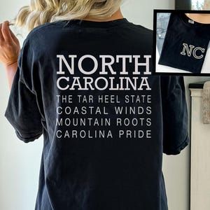 May include: Black t-shirt with white text reading "NORTH CAROLINA" and related phrases. An inset image shows a similar shirt with "NC" in gold lettering. The shirt is a casual wear item.