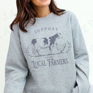 May include: Gray sweatshirt with a black and white cow and a chicken graphic. The text on the sweatshirt reads "Support Your Local Farmers".