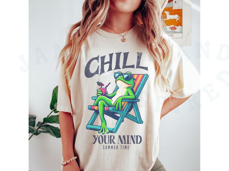 May include: Cream-colored t-shirt featuring a cartoon frog in sunglasses relaxing in a beach chair with a drink. The shirt has the words "CHILL YOUR MIND SUMMER TIME" in a distressed font.