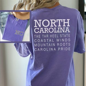 May include: A lilac t-shirt with the text "NORTH CAROLINA" and other phrases printed in white. An inset shows a matching shirt with "NC" embroidered. The shirt is a casual wear item.