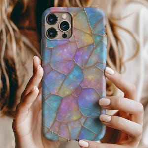 May include: A smartphone case with a colorful, stained-glass-like design. The case features a mosaic pattern in shades of blue, purple, yellow, and pink, with gold-colored outlines. The case is held by a person.