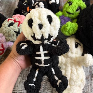 Op de afbeelding: Een gehaakt skelet-knuffeltje met een witte schedelkop met zwarte geborduurde gelaatstrekken en een zwart lichaam met witte details van de ribbenkast en ledematen. Het zachte figuurtje van getextureerd garen wordt voor andere knuffels gehouden.