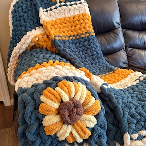 May include: A chunky knit throw blanket featuring a repeating pattern of large, three-dimensional sunflowers in shades of mustard yellow, cream, and brown, set against a deep navy blue background with thick, textured yarn loops throughout.