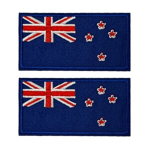 Op de afbeelding: Twee rechthoekige patches met de vlag van Nieuw-Zeeland. Het ontwerp toont de Union Jack in de linkerbovenhoek, met rode en witte sterren op een marineblauwe achtergrond. De patches hebben een marineblauwe rand.