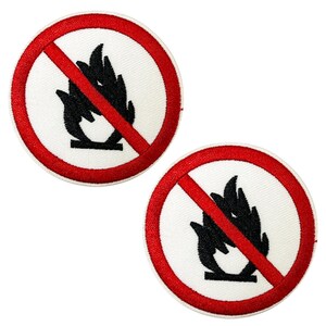 May include: Two circular embroidered patches featuring a white background, a red border, and a red diagonal line through a black flame symbol. These patches are likely safety or warning labels.