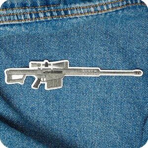 May include: An embroidered patch depicting a sniper rifle with a scope, in shades of grey and white. The patch is attached to blue denim fabric, highlighting the rifle's features. The patch is a decorative item.