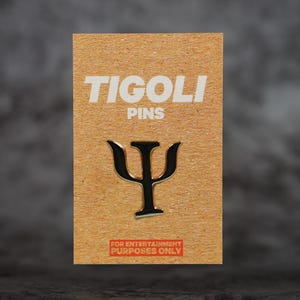 Può includere: Spilla nera e argento a forma di lettera greca psi, esposta su una scheda marrone. La scheda riporta la scritta "TIGOLI PINS" in lettere bianche in alto e "FOR ENTERTAINMENT PURPOSES ONLY" in rosso in basso.