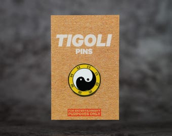 May include: A pin featuring a black and white Yin and Yang symbol, set within a yellow and black circular border. The pin is on a brown card with the text "TIGOLI PINS" and "FOR ENTERTAINMENT PURPOSES ONLY".