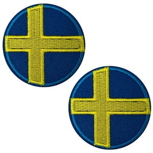 Op de afbeelding: Twee geborduurde patches met de vlag van Zweden. Elke patch heeft een blauwe cirkelvormige achtergrond met een gele Scandinavische kruis. Het kruis loopt door tot aan de randen van de cirkel. Geschikt voor kleding of accessoires.