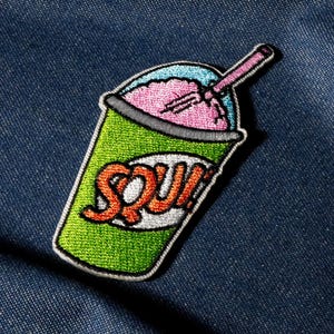 May include: Embroidered patch of a green, pink, and blue slushy drink with a pink straw. The word "SQUISH" is embroidered in orange and white on the front of the cup. The patch is set against a blue denim background.