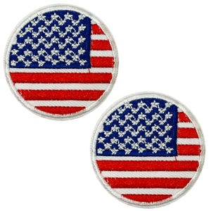 Op de afbeelding: Twee ronde geborduurde patches met de Amerikaanse vlag. Elke patch heeft een blauw veld met witte sterren en rood-witte strepen. De patches zijn omlijnd met een witte rand.