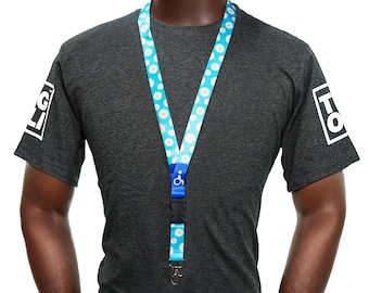 May include: A lanyard with a blue and white daisy pattern, a black clasp, and a silver-colored metal clip. The lanyard has a blue plastic piece with a white wheelchair symbol. The person is wearing a dark gray t-shirt with white text on the sleeves.