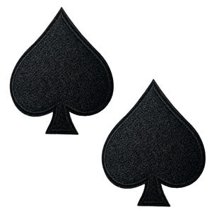 May include: Two black spade-shaped patches with a textured surface are shown against a white background. The patches are identical in shape and size, featuring a classic spade design. These patches are likely for clothing or accessories.