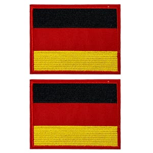 Op de afbeelding: Twee rechthoekige patches met het ontwerp van de Duitse vlag. Elke patch heeft een zwarte streep aan de bovenkant, een rode streep in het midden en een gele streep aan de onderkant, allemaal met een rode rand.