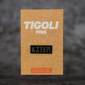 May include: A black rectangular pin with the word "ITEM" in white lettering, on a tan card. The card reads "TIGOLI PINS" at the top and "FOR ENTERTAINMENT PURPOSES ONLY" in red at the bottom.