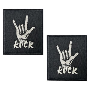 May include: Two square black patches with white embroidered hand gestures and the word "ROCK". The hand shows the rock and roll sign. These patches are likely for clothing or accessories.