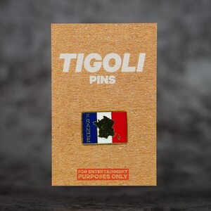 Op de afbeelding: Een rechthoekige pin met de Franse vlag en een kaart van Frankrijk. De pin is bevestigd op een kartonnen achtergrond met de tekst "TIGOLI PINS" en "FOR ENTERTAINMENT PURPOSES ONLY". De pin heeft de kleuren blauw, wit en rood.