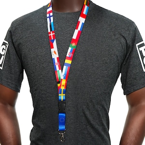 Peut inclure: Un cordon porte-badge avec des drapeaux de différents pays, dont le drapeau de l'UE, est porté autour du cou d'une personne. Le cordon est multicolore avec un fermoir en plastique noir et un crochet en métal. La personne porte un t-shirt gris foncé avec un logo blanc sur la manche.