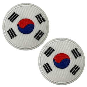 Può includere: Due toppe circolari con la bandiera sudcoreana. Ogni toppa ha uno sfondo bianco con un simbolo yin-yang rosso e blu al centro, circondato da quattro trigrammi neri. Le toppe sono ricamate con un bordo bianco.