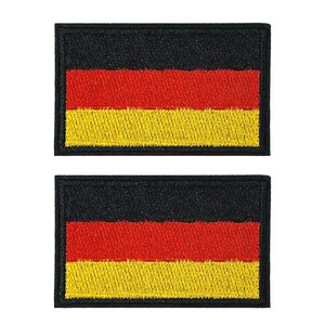May include: Two rectangular patches displaying the German flag. Each patch has a black border, with the flag's colours: black at the top, red in the middle, and yellow at the bottom. These patches are likely for clothing or accessories.