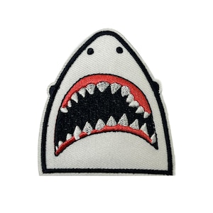 May include: Embroidered patch depicting a shark's open mouth with sharp white teeth and a red interior. The patch has a white background with a black outline. The design is a cartoon-style illustration of a shark's mouth.