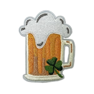 Peut inclure: Écusson brodé représentant un mug de bière avec une tête mousseuse et un trèfle vert. Le mug est rempli de bière ambrée et possède une anse blanche. L'écusson a une bordure grise et convient aux vêtements ou accessoires.